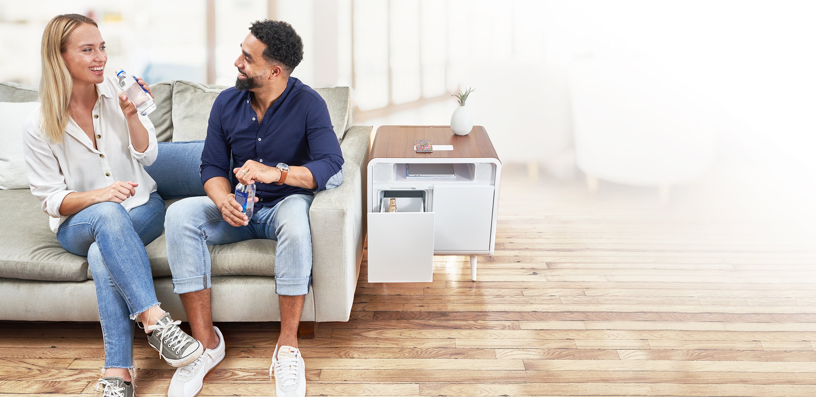 A woman and man sitting on a couch enjoying a cold beverage store in their Sobro side table