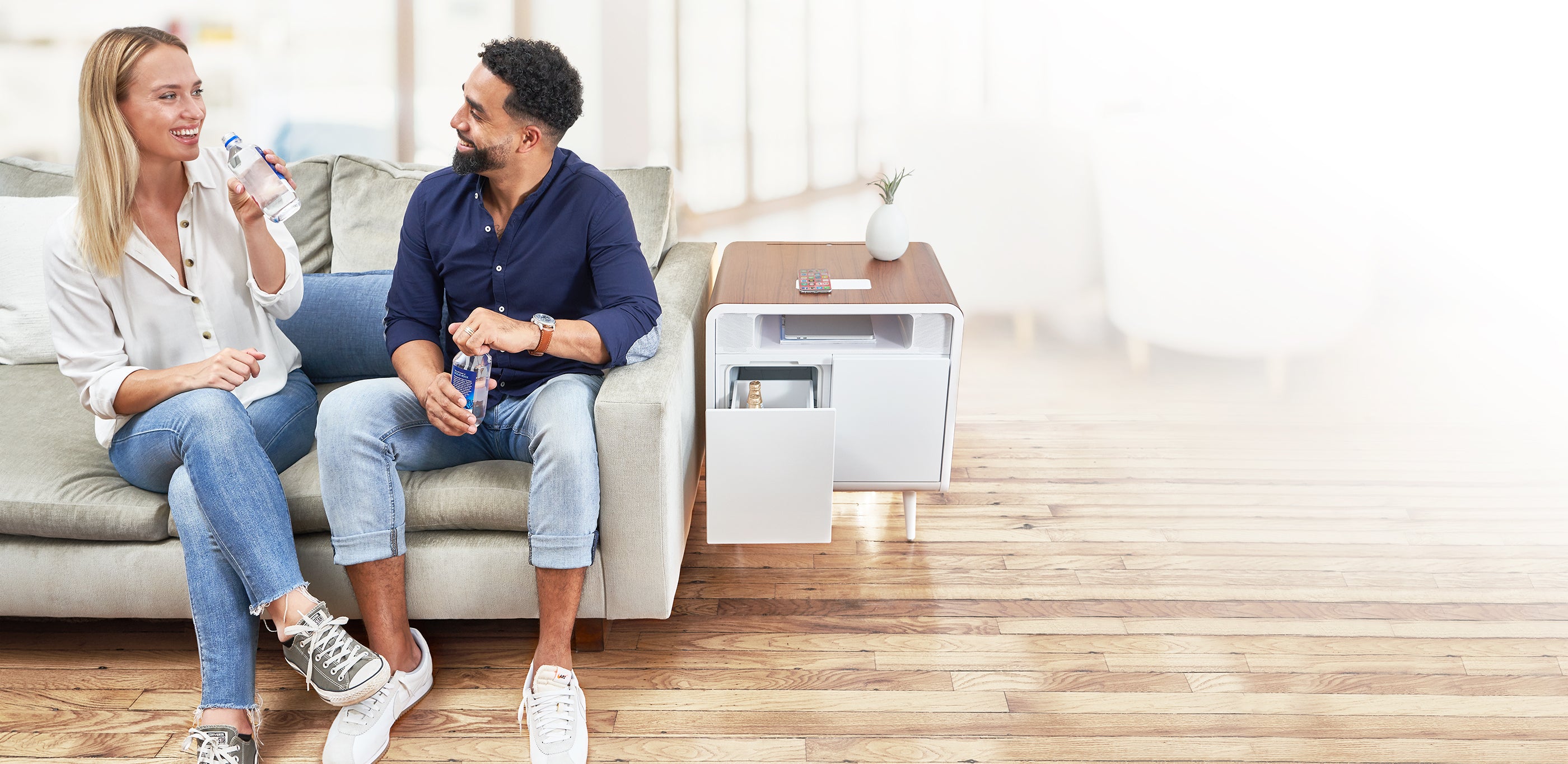 A woman and man sitting on a couch enjoying a cold beverage store in their Sobro side table 